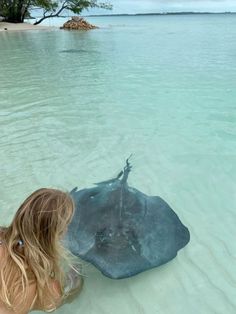 a woman sitting in the water next to a large stingper on top of a sandy beach