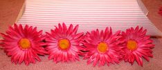 three pink flowers sitting on top of a bed next to a white and striped pillow