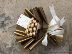 a wrapped gift box filled with chocolates on top of a stone floor next to a white ribbon