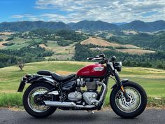 a red motorcycle parked on the side of a road next to a lush green hillside