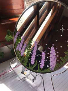 a mirror with purple flowers in it on a table next to a pen and paper