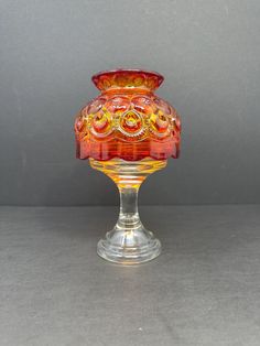 a red glass vase sitting on top of a table next to a gray wall and floor