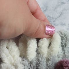 a hand with pink and white glitter on it next to a crocheted blanket