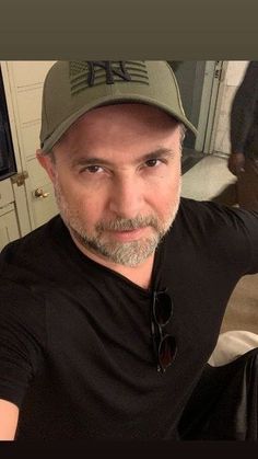 a man in a black shirt and hat taking a selfie with his cell phone