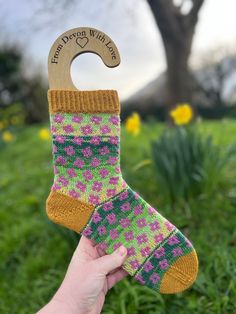 a hand holding up a wooden shoe shaped like a sock with pink and green designs on it