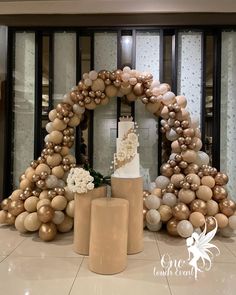 a wedding cake surrounded by balloons and flowers in front of a large window with an arch