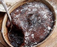 a bowl filled with cake sitting on top of a wooden table next to a fork