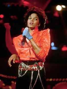 a woman in an orange shirt and black pants holding a microphone while standing on stage