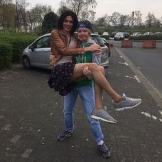 two people standing in the middle of a parking lot, one holding the other's leg