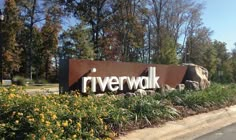 the riverwalk sign is located in front of some flowers and trees with yellow flowers around it