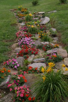 a garden with flowers and rocks on the side of it in front of a grassy field