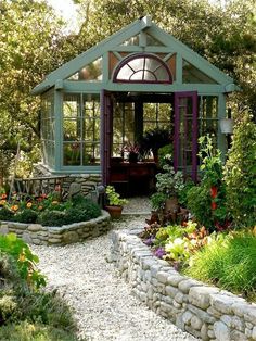 a garden shed with lots of plants and flowers in the front yard, surrounded by rocks