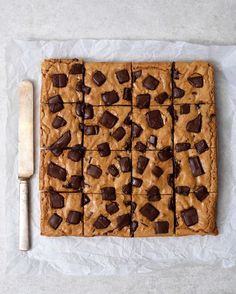 chocolate chip cookie bars cut into squares on top of parchment paper next to a knife