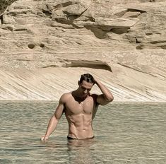 a shirtless man standing in the water with his hand on his head