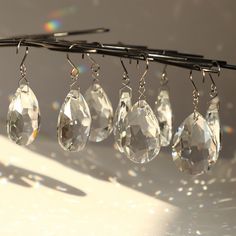 several pairs of crystal earrings hanging from a metal hook on a white surface with sunlight shining through the window