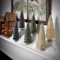 christmas trees are lined up on a mantle in front of a framed holiday card and birdhouse