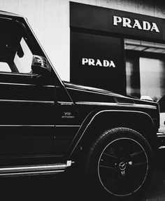 a black and white photo of a jeep parked in front of a prada store