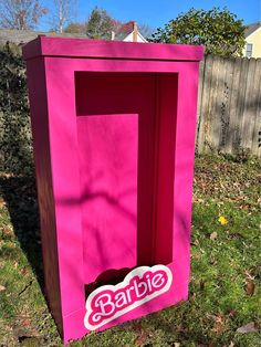 a pink cardboard box with the word barbie on it in front of a fence and yard