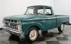 an old green pickup truck is parked on a checkered floor