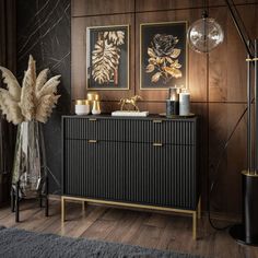 a black and gold sideboard with two pictures on the wall next to it in a living room