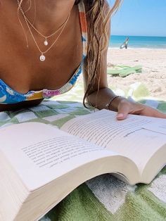 a woman reading a book on the beach with her head resting on an open book