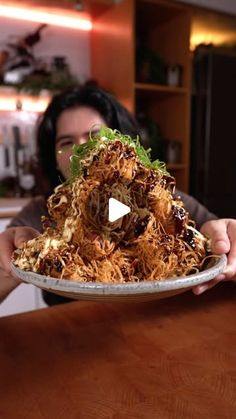 a woman holding a plate with food on it in front of her face and the video is out