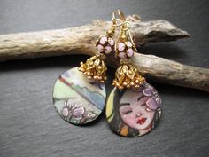 These earrings feature wonderful illustrated enameled copper charms by TheDreamCatchersCo in Bulgaria. One charm depicts a serene brunet girl with lilac flowers in her hair, while the other depicts the bucolic country view.  Above the charms are a double layer of soft pink enamel flower beads caps followed by ornate gold bead caps. Next are rhinestone spacers set in gold. These are topped by pink disco ball beads. Small brass beads finish off these bohemian country life earrings, which hang from simple gold ear wires and measure 2.25 inches long. These earrings will be sent to you attractively packaged in a gift box with ribbon. You can check out more of my one-of-a-kind creations here: http://www.etsy.com/shop/ThreeWishesStudio. Collectible Bohemian Jewelry With Artistic Design, Whimsical Enamel Jewelry For Jewelry Making, Whimsical Hand Painted Enamel Jewelry, Whimsical Hand Painted Gold Earrings, Whimsical Hand Painted Dangle Jewelry, Bohemian Hand Painted Enamel Jewelry, Bohemian Hand Painted Gold Earrings, Bohemian Gold Hand Painted Earrings, Hand Painted Bohemian Enamel Jewelry