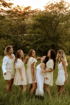 a group of young women standing next to each other in tall grass with trees in the background