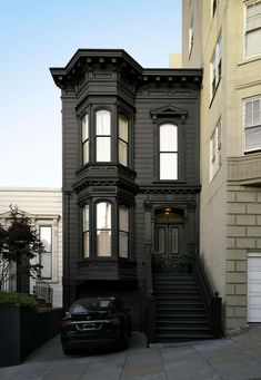 a black car parked in front of a house on a street next to tall buildings