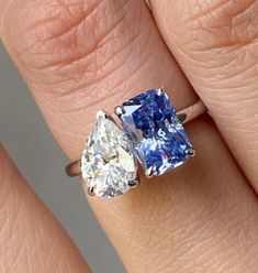 a woman's engagement ring with two pear shaped blue and white diamonds on it