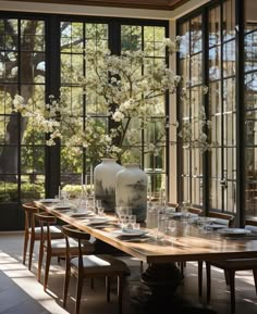 a dining room table with vases and glasses on it in front of large windows