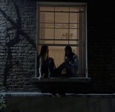 two people sitting on a window sill at night