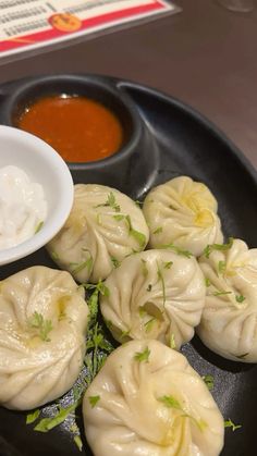 some dumplings are on a black plate with dipping sauce