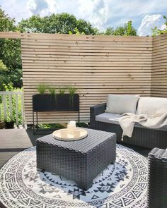 an outdoor living area with wicker furniture and rugs on the floor, in front of a wooden fence