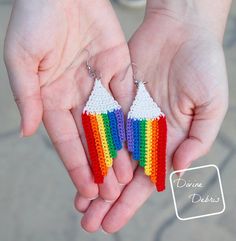 a pair of rainbow earrings in the palm of someone's hand with their hands