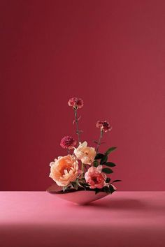 an arrangement of flowers in a bowl on a pink surface