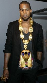 a man wearing a gold necklace with an egyptian mask on it's chest and black jacket