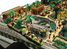 a lego model of a train station with lots of people and trees on the tracks