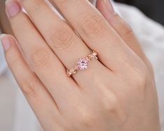 a close up of a person's hand holding a ring with two pink stones