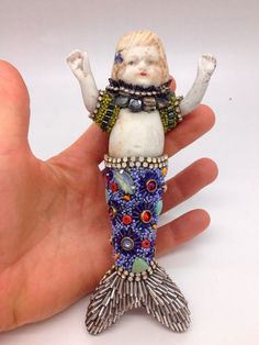 a hand holding a small figurine in the shape of a mermaid on it's back