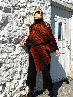 "Fall Knit Steampunk Ruffle Wrap | Boho Alpaca Black Orange Poncho, Wool Poncho Cape For Women This flirty, ruffled, alpaca wool blend hand-knitted wrap in black and burnt orange tons, is light and warm. It is a four-season piece and is ideal for layering.  The colour palette of this versatile shawl is definitely jeans friendly.  STYLE This dressy/casual piece is an excellent travel companion.  Works well with jeans, leggings, dress pants or over a solid dress adding a flowy elegance of a shawl. Endless in its versatility and fits most sizes make it a great gift idea. Material: Alpacas Wool Blend WAYS TO WEAR SEE FAQ's FOR WAYS TO WEAR AS A SHAWL, FITTED LOOK, BELTED LOOK AND SCARF. SIZING Length is approx. 30\" Fits sizes S- 3xl Please inquire about larger sizes Our model Elana is size 8 One Size Cape For Fall Festival, Fall Festival Cape Poncho, Black Cape For Fall Festivals, Acrylic Poncho Shawl For Fall, Black Fall Festival Cape, Acrylic Shawl Poncho For Fall, Bohemian Black Poncho For Fall, One Size Acrylic Poncho For Fall, Bohemian Knitted Poncho For Fall