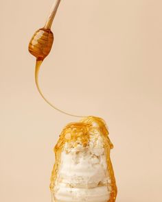 a honey dripping from a spoon into a jar filled with ice cream and whipped cream