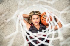 a woman holding a basketball in front of a net with her hands behind her head