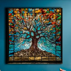 a stained glass window with a tree in the center on a blue wall behind it