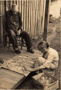 an old black and white photo of two people sitting on a porch playing with paper