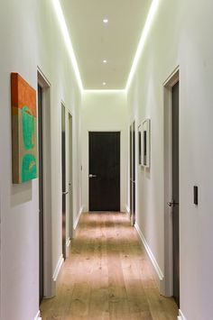 a long hallway with white walls and wooden floors is lit by recessed lighting above the doors