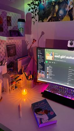 a laptop computer sitting on top of a desk next to a lit up book and candle