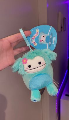 a hand holding a blue stuffed animal with a tag on it's ear,