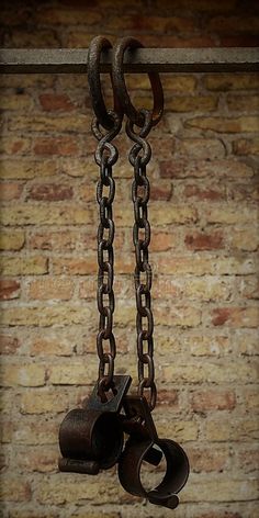 an old pair of chains hanging from a hook on a brick wall in front of a window