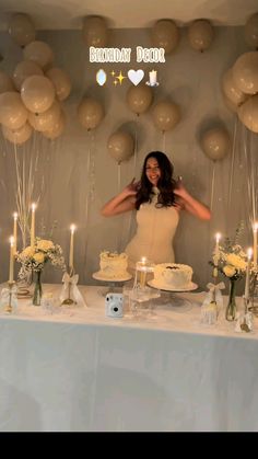 a woman standing in front of a table filled with cake and candles, surrounded by balloons